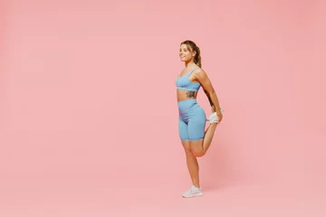 Wandcirkels tuinposter Full body young sporty athletic fitness trainer woman wear blue tracksuit spend time in home gym train do stretch legs exercise isolated on pastel plain light pink background. Workout sport concept. © ViDi Studio
