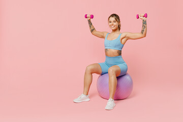 Naklejka na ściany i meble Full size young strong sporty athletic fitness trainer instructor woman wear blue tracksuit spend time in home gym sit on fitball isolated on pastel plain light pink background. Workout sport concept.