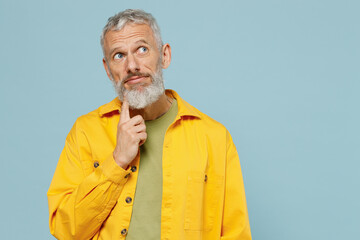 Elderly wistful minded gray-haired mustache bearded man 50s wearing yellow shirt look aside on workspace area mock up isolated on plain pastel light blue background studio. People lifestyle concept.