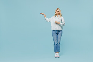 Full body elderly woman 50s wear casual striped shirt looking camera point finger on gesture scale measure height isolated on plain pastel light blue color background studio People lifestyle concept.