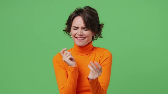Happy young brunette woman 20s wear orange shirt dance clenching fists waving rising expressive gesticulating hands fooling around have fun celebrate isolated on plain green background studio portrait