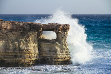 water splashing wave and hole in cliff at famous sea caves at cape greco peninsula, cyprus