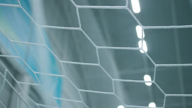 Blurred view of gym ceiling with glowing led lamps through white mesh of football gate in contemporary sports complex closeup