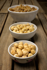 Hazelnuts, cashew nuts and walnuts in different jars on a wooden table in a top view and in a dark environment.