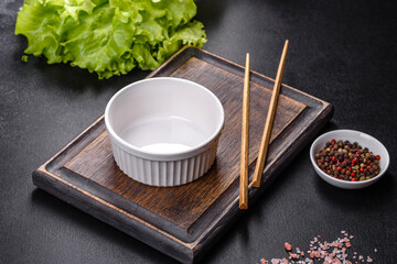 An empty white bowl and sticks on a wooden cutting board