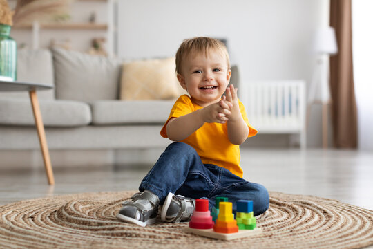 Adorable toddler boy playing with educational wooden toy at home, clapping hands and smiling, sitting on carpet