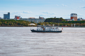 Chinese pleasure boat on the Amur River in autumn against the background of buildings in Heihe, China. View from the embankment of the city of Blagoveshchensk, Russia.