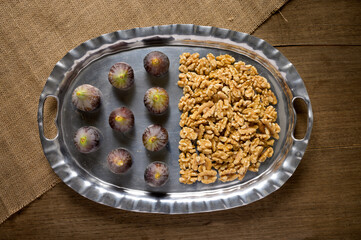 Figs and walnuts on a silver platter in the wood background in a dark setting