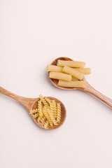 Two wooden spoons with uncooked pasta. Different types of pasta