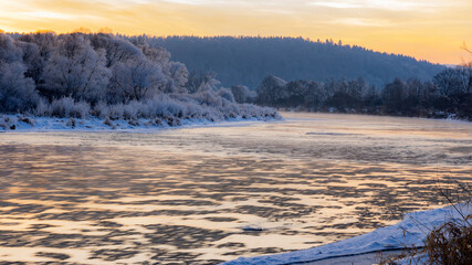 Winter sunset view of the San river and snow-covered trees in Poland