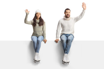 Fototapeta premium Young man and woman with ice skates sitting on a blank panel and waving