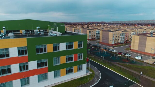 Contemporary bright color building with parking lots and large playground in city district on cloudy day aerial view