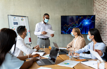 Covid Coworking. Black Businessman Wearing Medical Mask Having Office Meeting With Colleagues