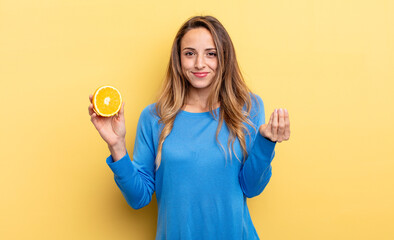 pretty woman making capice or money gesture, telling you to pay holding half orange