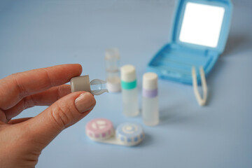 Hand holds a lens and ophthalmic set for hard contact lenses on a blue background.