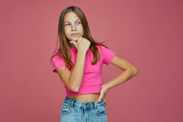 Pensive little child girl touch chin thinking or considering, making decision imagining idea on pink studio background