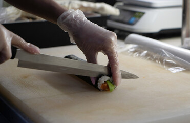 Photo of the process of cutting sushi and rolls from rice, cucumbers, red fish, seaweed and avocado. Male chef hands in gloves