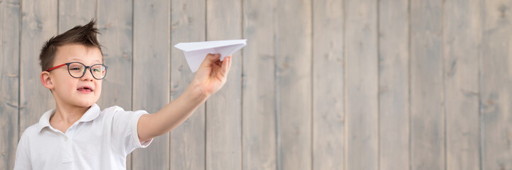 cute schoolboy making and launching a paper airplane wearing glasses and a white t-shirt on wooden...
