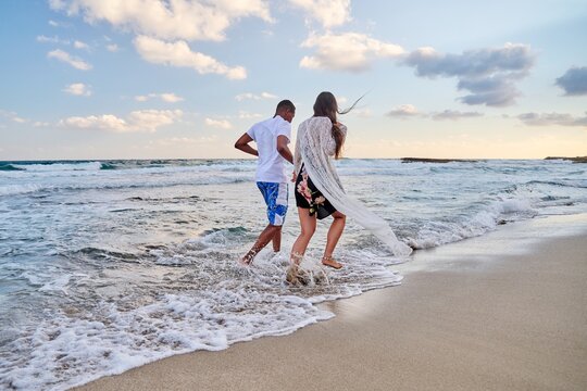 Happy couple running together on beach on summer day, back view