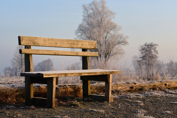 An old wooden bench stands on frosty ground in winter and is covered with hoarfrost in a wintry...