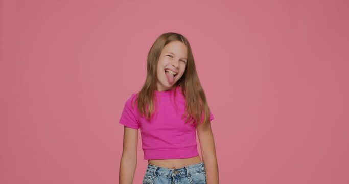 Funny child girl showing tongue teasing making faces fooling having fun on pink background. Playful childish mood
