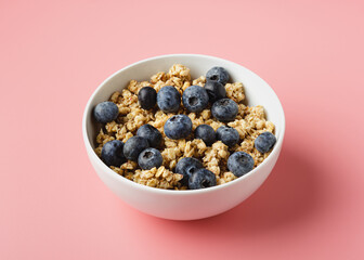 Granola with blueberry in bowl on pink background.