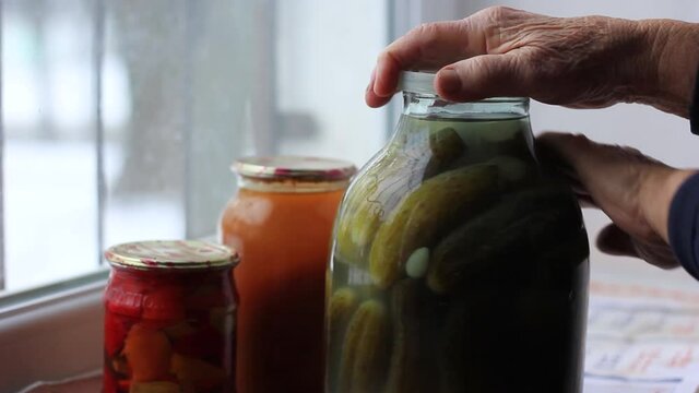 An elderly woman wipes a jar of pickles with her hand.