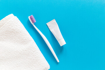 Flatlay of white towel and toothbrush in a box with a blue background and copy space for your text. Morning routine during travel