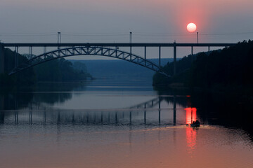 sunset on the river, sun path and silhouette of people in a boat. railway bridge over the river in...