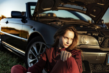 Fototapeta na wymiar A beautiful girl near a car broken down in a field, a retro convertible
