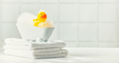A miniature bubble bath, yellow rubber duck and white towels on bathroom countertop, children bath...