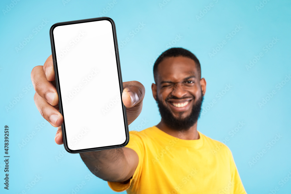 Poster mobile app advertisement. smiling black man showing smartphone with empty screen, winking on blue ba
