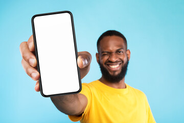 Mobile app advertisement. Smiling black man showing smartphone with empty screen, winking on blue...