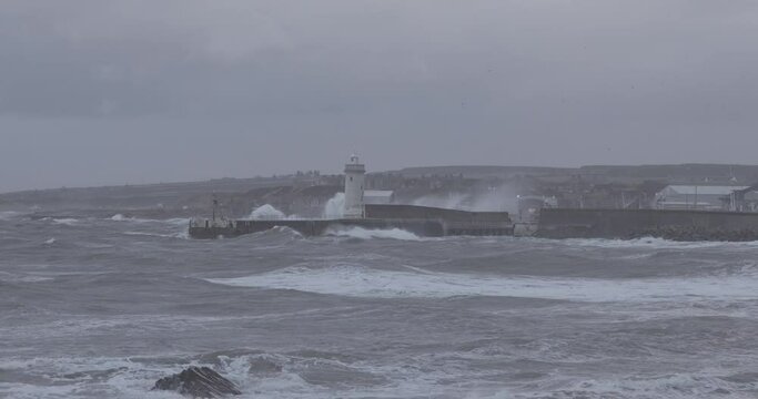 A footage scenic lighthouse at the Buckie, Moray, Scotland port entrance during a major storm with big waves crashing on it under a grey stormy sky