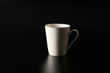 A white mug with a golden rim on top and a stripe on the handle on a black background. Copy space.