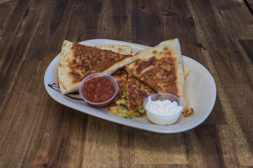 Cheese quesadilla cut up on a plate with sour cream and salsa 