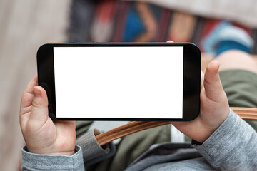 Boy's toddler hands holdingphone on home background. Child's hands hold black smartphone and...