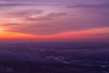 Epic red sunset over the rocks and stones of Ural mountains covered with snowy pines.