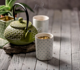 Still life of a cup of tea with a box of herbal tea and a traditional green metal tea pot in the background.