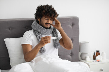 Ill indian guy with scarf around neck checking temperature