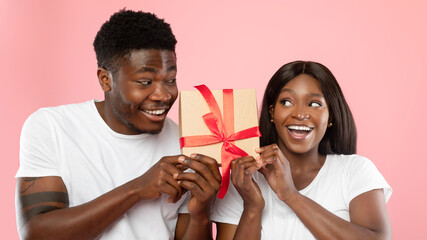 Happy black couple shaking gift box at pink studio