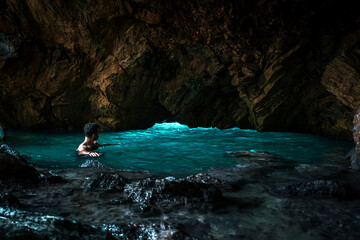 young man looking at light in pool inside dark natural cave