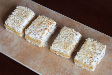 Several individual servings of Crusted in a row on an abstract textured, pastel-colored tray. Traditional sweet puff pastry dessert with cream and meringue covered with chopped almonds and icing sugar