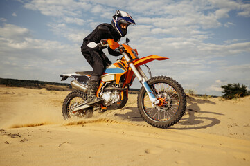 Fototapeta na wymiar Professional motocross rider driving on sand dune