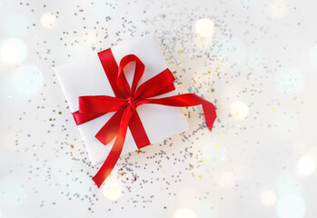 Gift box wrapped in white paper with a red bow on festive light background. Copyspace for your text. Flat lay style. Christmas, New Year or birthday celebration concept. Web element for postcard