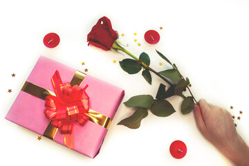The child's hand holds a red rose, candles and a pink gift box with a red bow are lying next to it. White background. Valentine's day, wedding, mother's day, birthday. Flat lay.