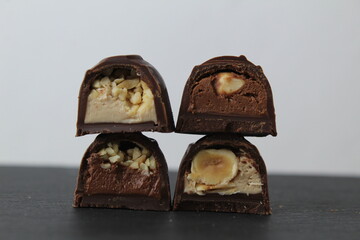 four chocolates in frosted nuts whole crushed peanuts hazelnuts dark light chocolate cream pralines close-up lie on top of each other