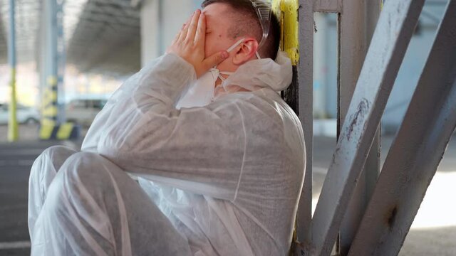 Despair healthcare worker in white covid protective overalls.Tired Male caucasian doctor grabs his head cower in depression during coronavirus pandemic Paramedic overworked cry covered face with hands