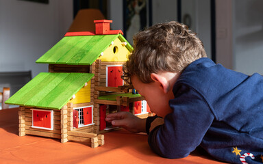 Obraz premium Caucasian child boy playing with a vintage wooden log cabin on a table, a creative wood construction toy.
