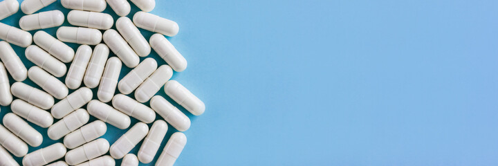 Close-up white pharmaceutical pills with colostrum on blue background. Horizontal banner, selective...